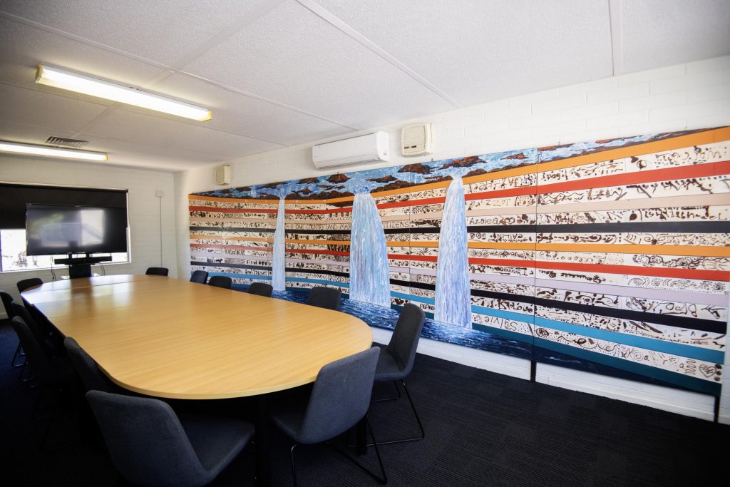 Conference room with wooden table, black chairs, wall-mounted TV, and shelved storage units containing files.