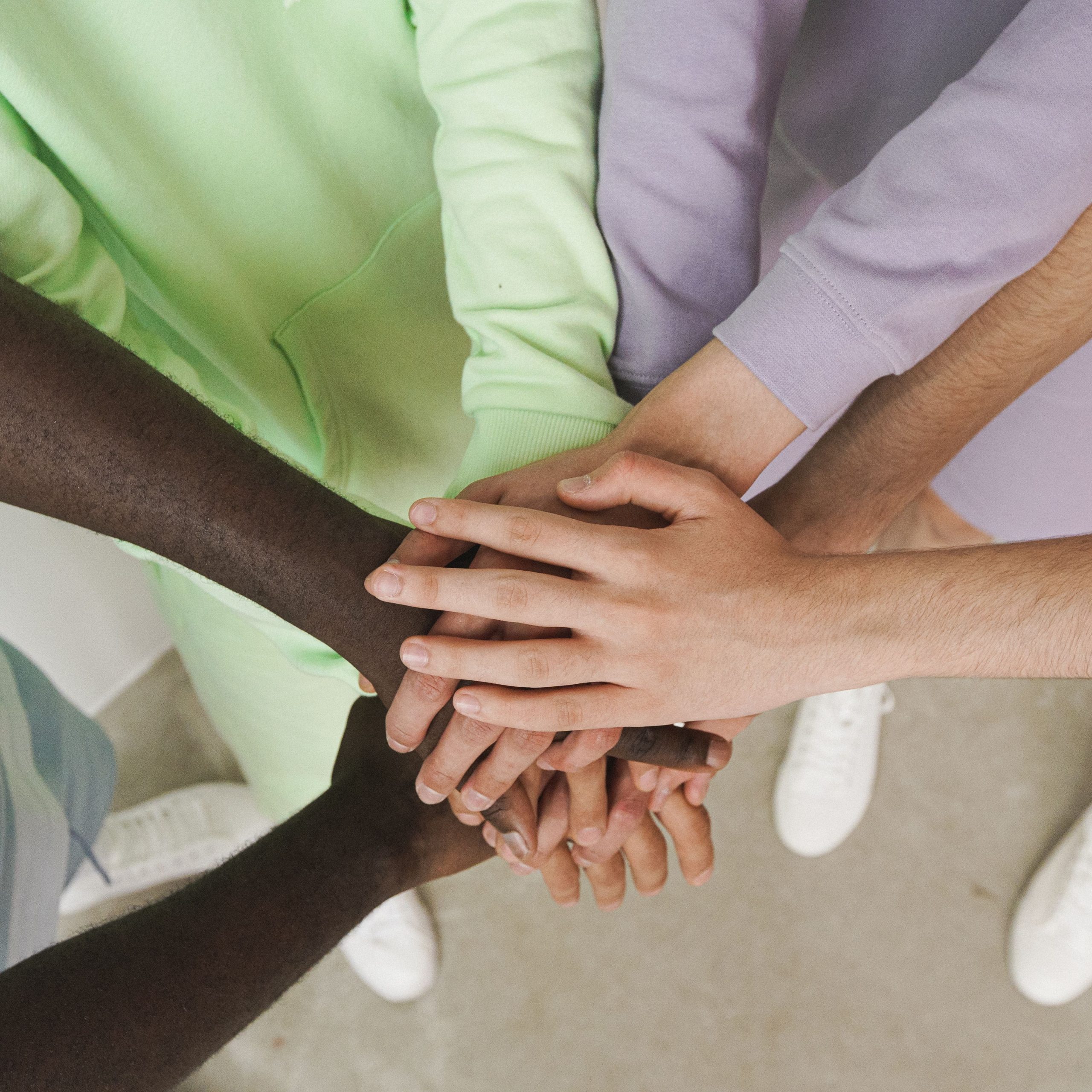 Multiple hands of different skin tones stacked together in a group huddle gesture.